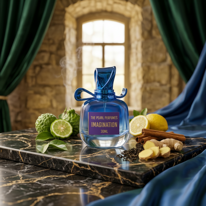 A 30ml bottle of 'The Pearl Perfumes: Imagination' in a vibrant blue glass bottle with a bow detail, displayed on a black marble tray with lemons, cinnamon, ginger, and green leaves. The background features a stone wall, a window, and draped green and blue curtains.